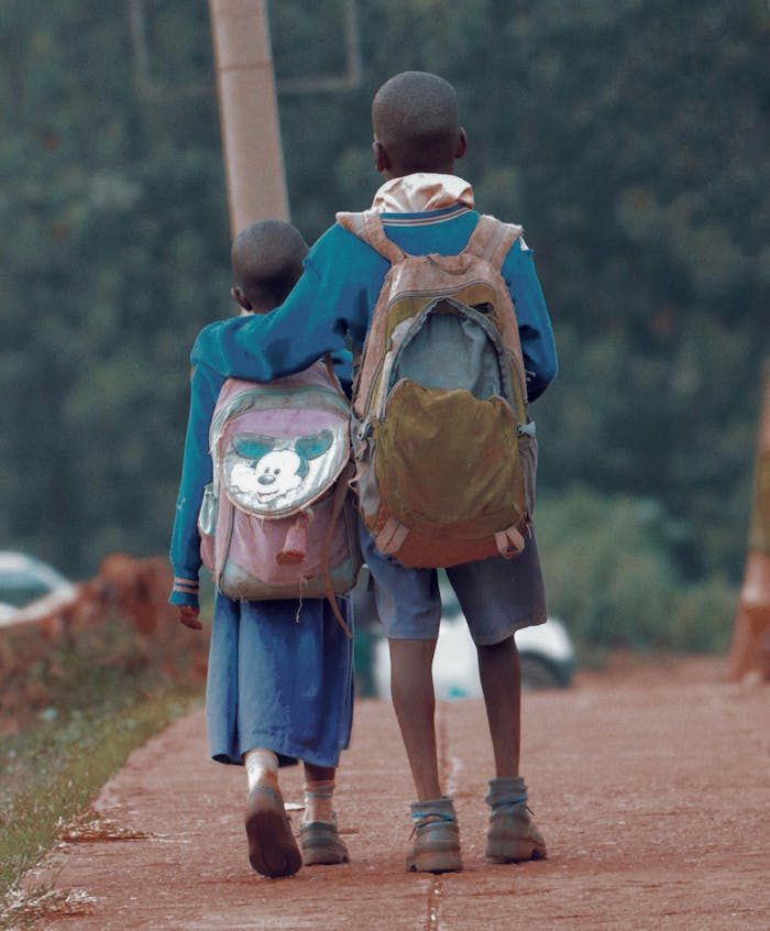 Two children with backpacks walking down a path in Kisii, Kenya, symbolizing education.
