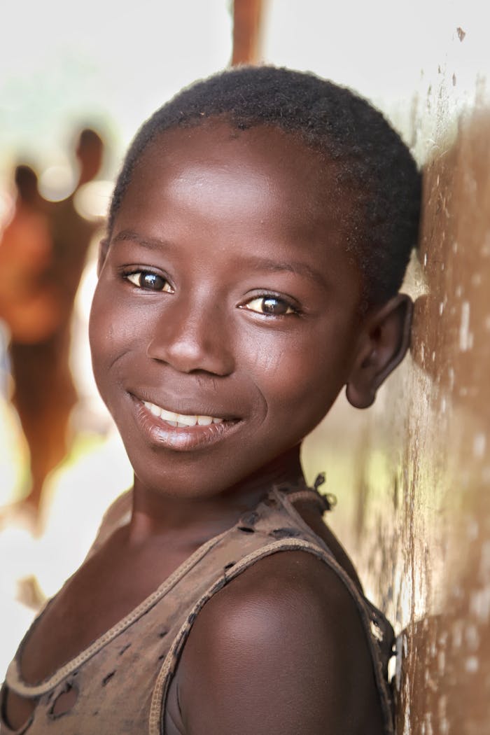 Close-up portrait of a smiling African child leaning on a wall in natural light.
