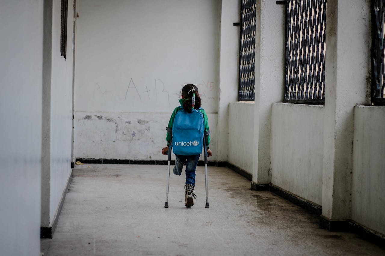 A young girl with a backpack and crutches walking indoors, symbolizing resilience.